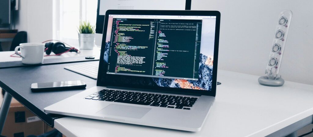 A MacBook with lines of code on its screen on a busy desk