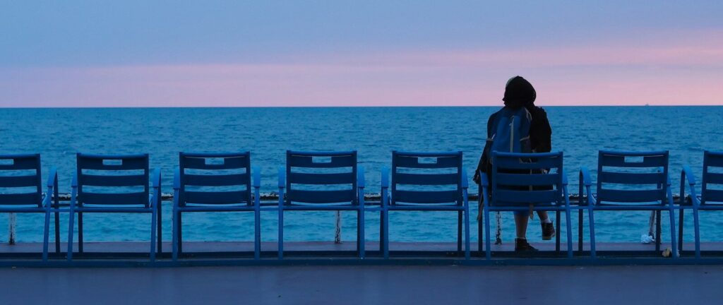 person sitting on blue wooden bench on beach during daytime